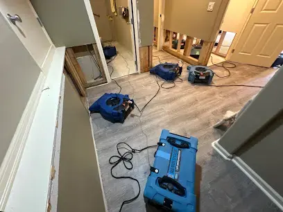 Air movers and a dehumidifier drying a hallway with the lower walls opened after a Sammamish water leak