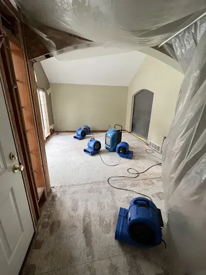 Air movers drying a carpeted room sealed off with plastic containment