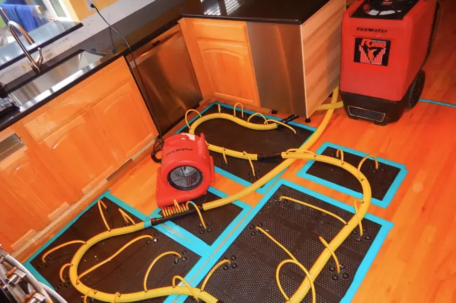 Dehumidifier and drying hoses on mats across a hardwood kitchen floor during a Sammamish water damage dry-out