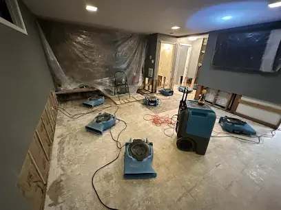 Air movers and a dehumidifier drying a room with plastic sheeting on the walls after a water leak