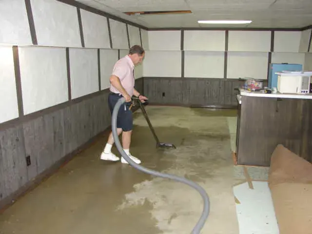 Technician extracting standing water from a finished basement floor with a wand and hose in Sammamish, WA